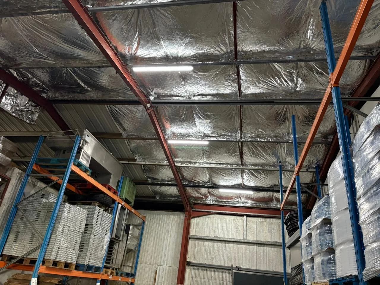 Vue intérieure d'un entrepôt logistique avec charpente métallique orange et toit en isolation aluminium réfléchissante